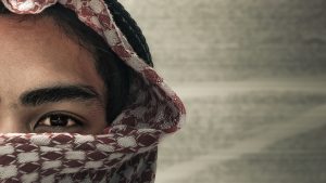 A man partially covered by a keffiyeh, evoking themes of identity, conflict, and radicalization.